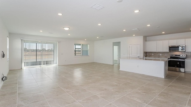 kitchen featuring light tile patterned flooring, tasteful backsplash, a center island with sink, stainless steel appliances, and white cabinets