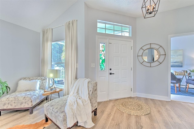 foyer with light wood-type flooring, vaulted ceiling, a textured ceiling, and a notable chandelier