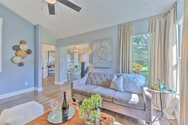 living room with hardwood / wood-style flooring, vaulted ceiling, a textured ceiling, and ceiling fan with notable chandelier