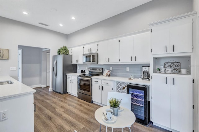 2309 Mooney Pl, Sun City Center, FL 33573 - kitchen with appliances with stainless steel finishes, white cabinetry, light countertops, wine cooler, and light wood-style flooring