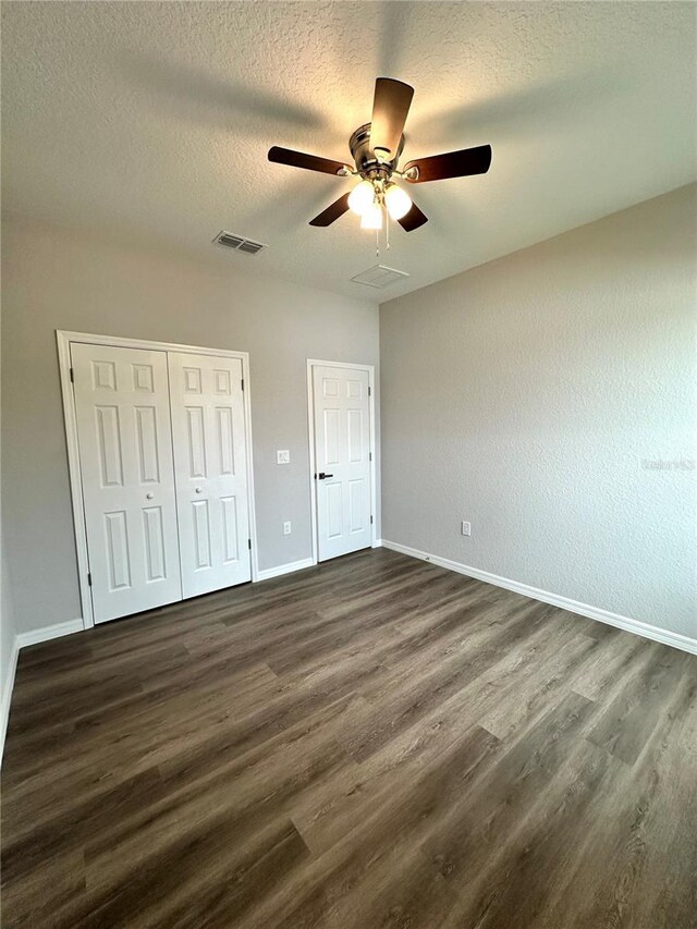 unfurnished bedroom featuring ceiling fan, a closet, a textured ceiling, and dark wood-type flooring