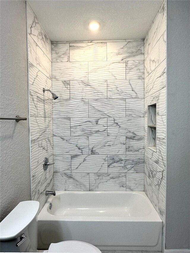 bathroom featuring a textured ceiling, toilet, and tiled shower / bath