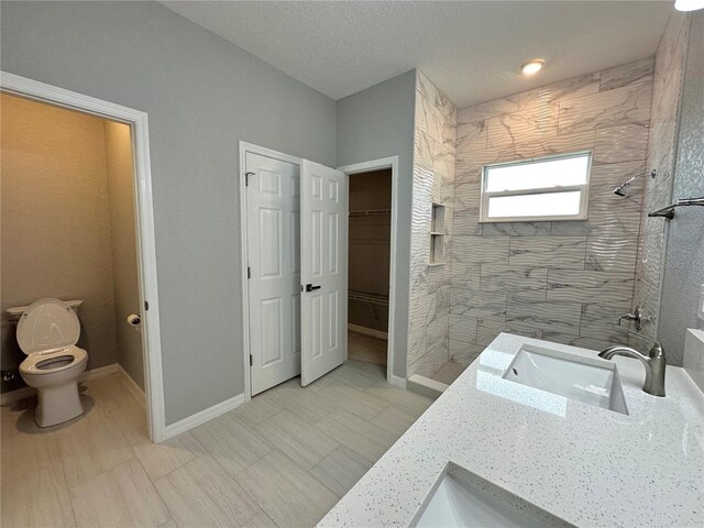 bathroom with tiled shower, a textured ceiling, tile patterned flooring, vanity, and toilet