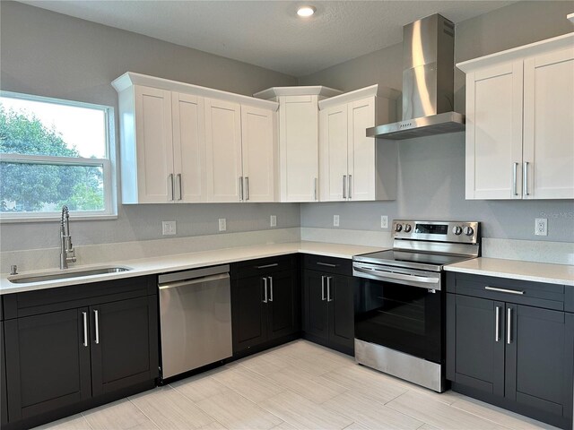 kitchen with sink, light tile patterned floors, stainless steel appliances, wall chimney range hood, and white cabinets