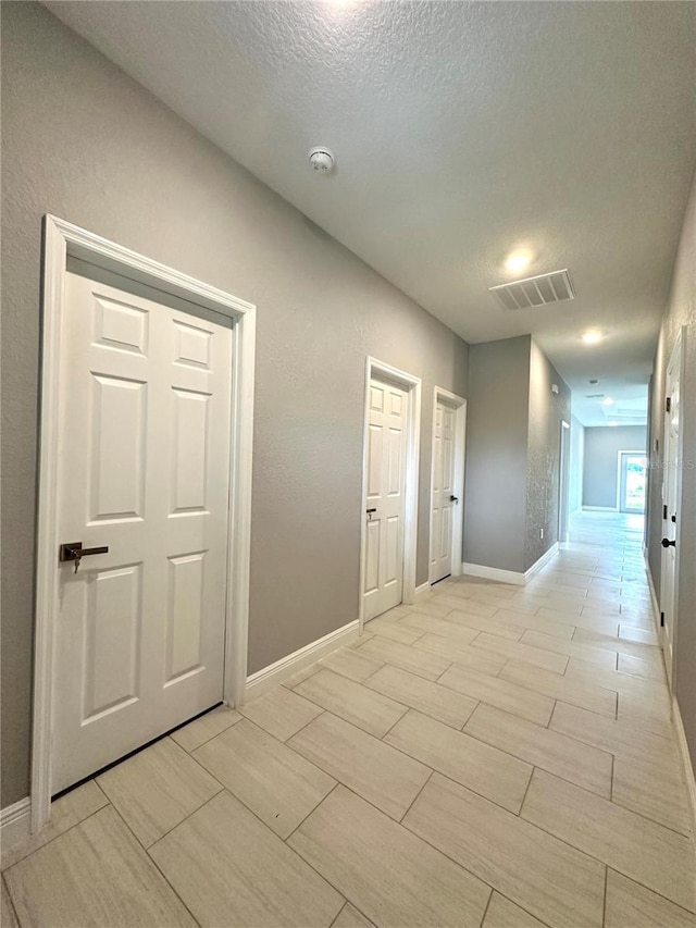 corridor with a textured ceiling and light tile patterned flooring