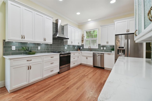 kitchen featuring appliances with stainless steel finishes, white cabinets, ornamental molding, and wall chimney range hood