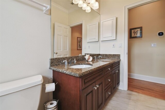 bathroom with toilet, ornamental molding, vanity, and wood-type flooring