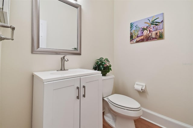 bathroom with toilet, wood finished floors, vanity, and baseboards