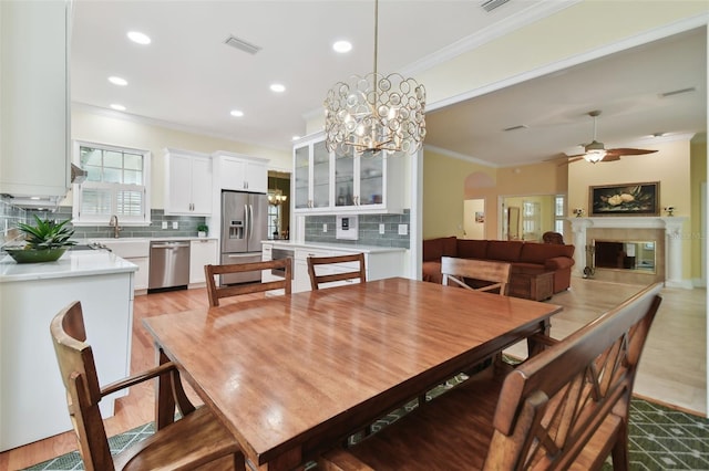 dining room featuring visible vents, arched walkways, a glass covered fireplace, ornamental molding, and ceiling fan with notable chandelier