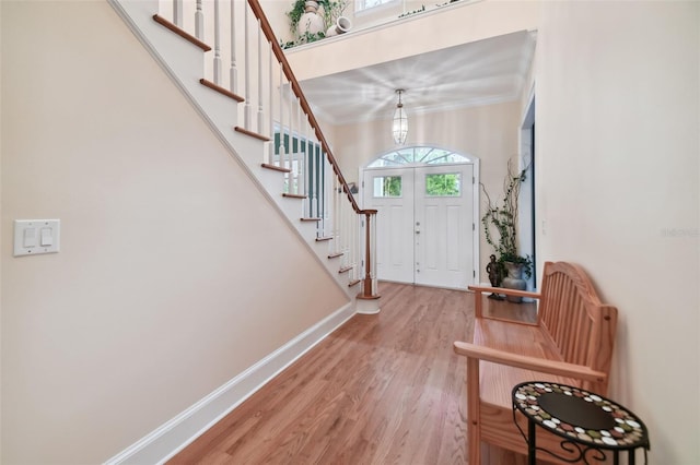 foyer with ornamental molding, light wood finished floors, baseboards, and stairs