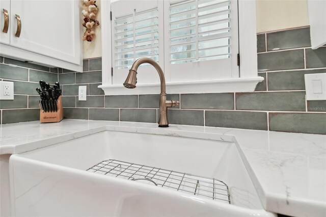 interior details with sink, white cabinets, backsplash, and light stone counters