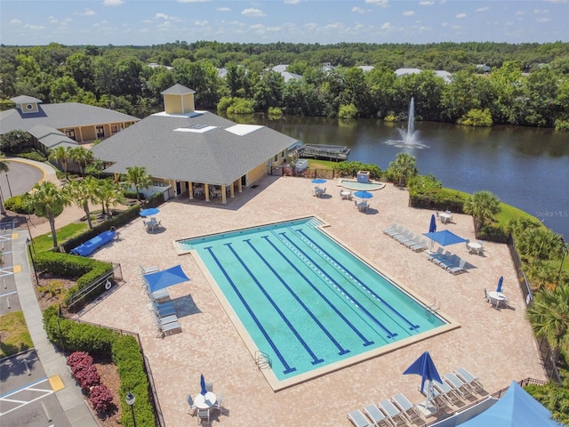 pool with a patio area, a water view, and a view of trees