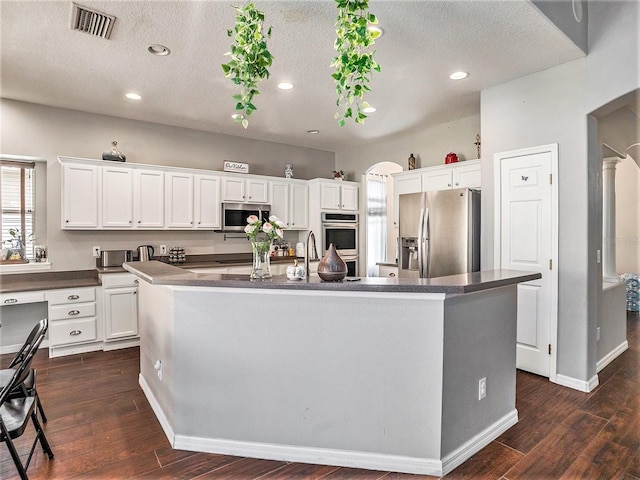 kitchen featuring a textured ceiling, stainless steel appliances, dark wood-type flooring, a center island with sink, and white cabinets