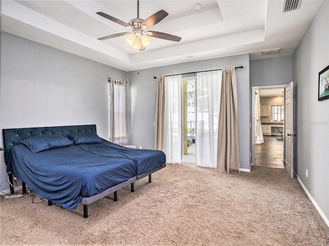 carpeted bedroom with ceiling fan and a raised ceiling