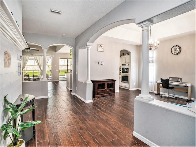 interior space with dark wood-type flooring, ceiling fan with notable chandelier, and decorative columns