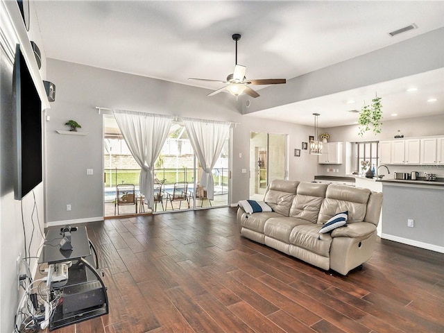 living room with ceiling fan with notable chandelier, dark hardwood / wood-style flooring, and sink