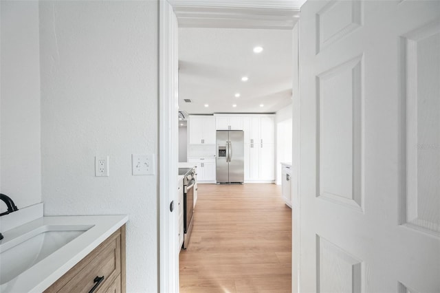 interior space with light wood finished floors, a textured wall, a sink, and recessed lighting