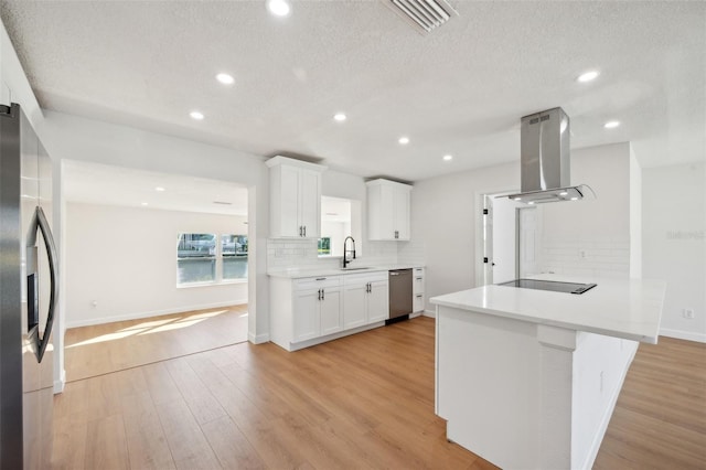 kitchen featuring light wood finished floors, visible vents, island range hood, appliances with stainless steel finishes, and backsplash