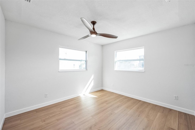 unfurnished room featuring a healthy amount of sunlight, a textured ceiling, baseboards, and wood finished floors