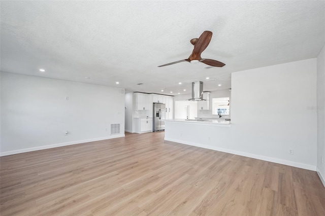 unfurnished living room with ceiling fan, a textured ceiling, light wood-style flooring, visible vents, and baseboards