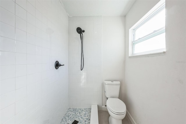 bathroom with toilet, baseboards, and a tile shower