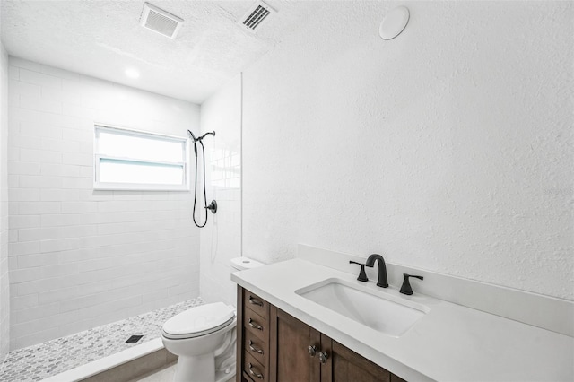 bathroom with a textured ceiling, toilet, vanity, visible vents, and a stall shower