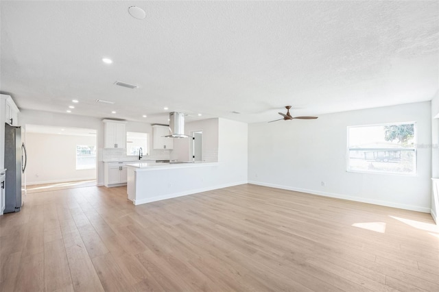 unfurnished living room with light wood-style floors, a textured ceiling, baseboards, and a ceiling fan