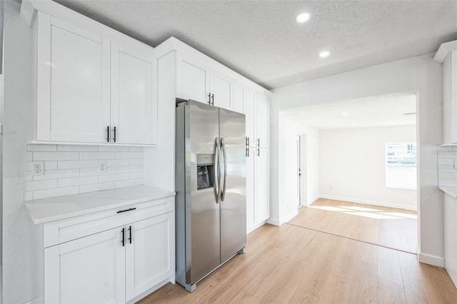 kitchen featuring white cabinets, decorative backsplash, light wood-style flooring, light countertops, and stainless steel refrigerator with ice dispenser