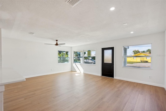 interior space featuring baseboards, visible vents, light wood-style flooring, and a textured ceiling