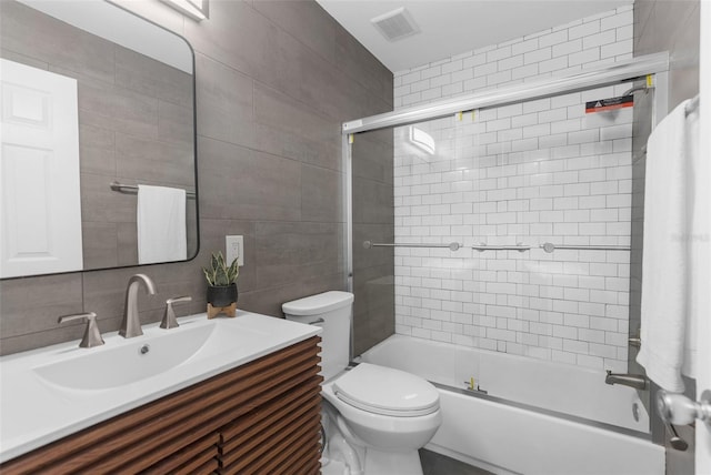 full bathroom with combined bath / shower with glass door, vanity, tasteful backsplash, tile walls, and toilet