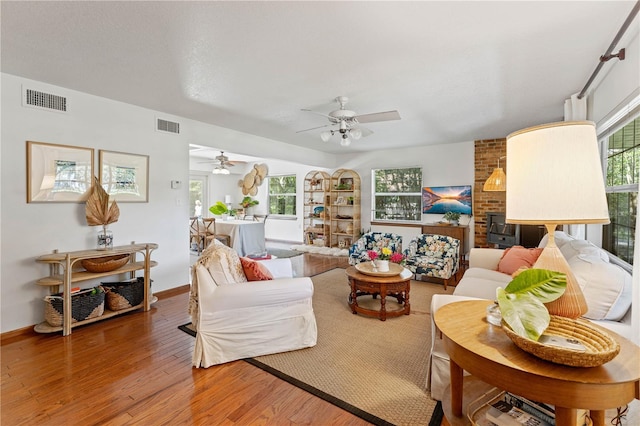 living room with a fireplace, brick wall, ceiling fan, and hardwood / wood-style flooring