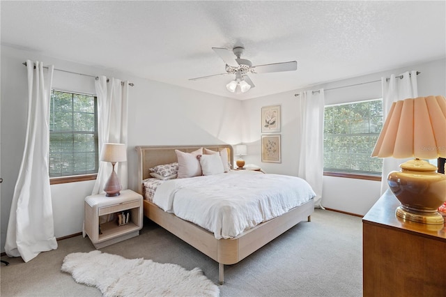 bedroom with a textured ceiling, ceiling fan, multiple windows, and light carpet