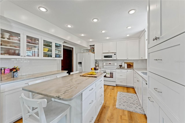 kitchen with a kitchen breakfast bar, white appliances, light hardwood / wood-style floors, and decorative backsplash