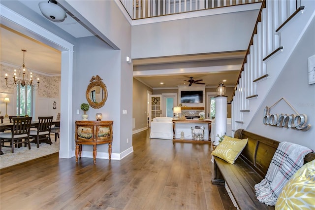 foyer with wood-type flooring, ceiling fan with notable chandelier, and ornamental molding