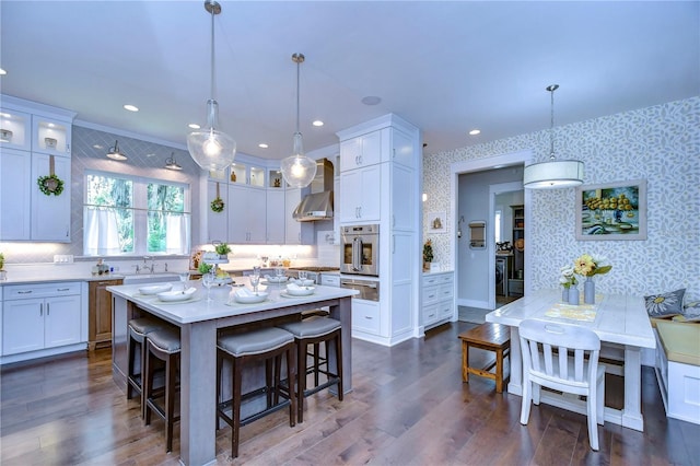 kitchen with white cabinetry, wall chimney range hood, dark hardwood / wood-style floors, oven, and a kitchen island