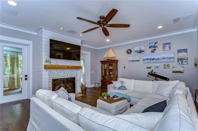 living room featuring a tiled fireplace, ceiling fan, dark hardwood / wood-style floors, and ornamental molding