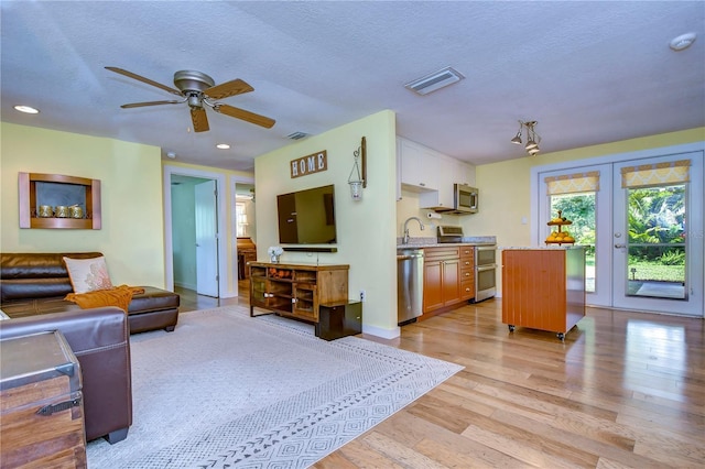 living room with ceiling fan, sink, light hardwood / wood-style floors, and a textured ceiling