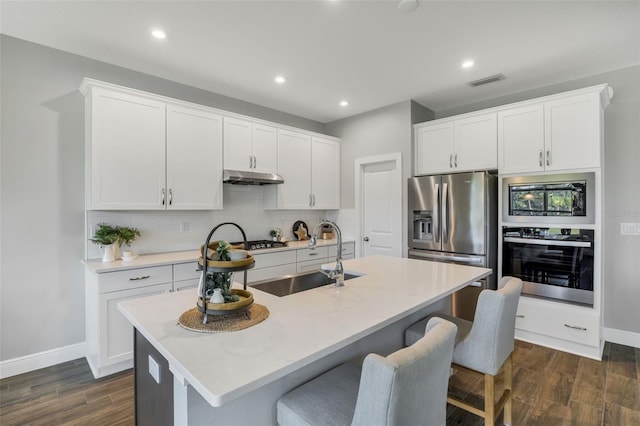 kitchen with dark wood-type flooring, a center island with sink, stainless steel appliances, and sink