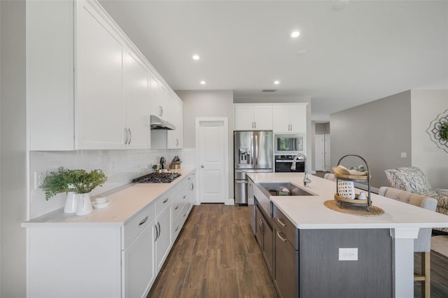 kitchen with backsplash, a kitchen island with sink, dark hardwood / wood-style flooring, white cabinetry, and stainless steel appliances