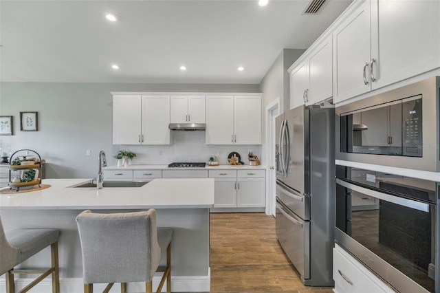 kitchen featuring white cabinets, stainless steel appliances, light countertops, under cabinet range hood, and a sink