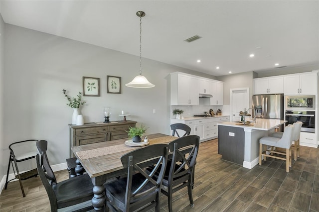 kitchen featuring stainless steel appliances, white cabinetry, light countertops, an island with sink, and decorative light fixtures