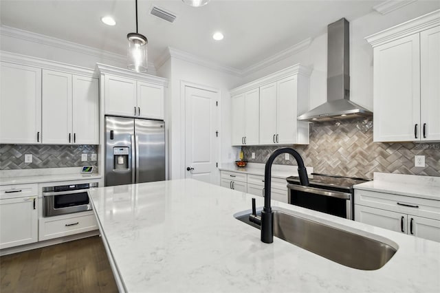 kitchen featuring hanging light fixtures, sink, appliances with stainless steel finishes, white cabinets, and wall chimney exhaust hood