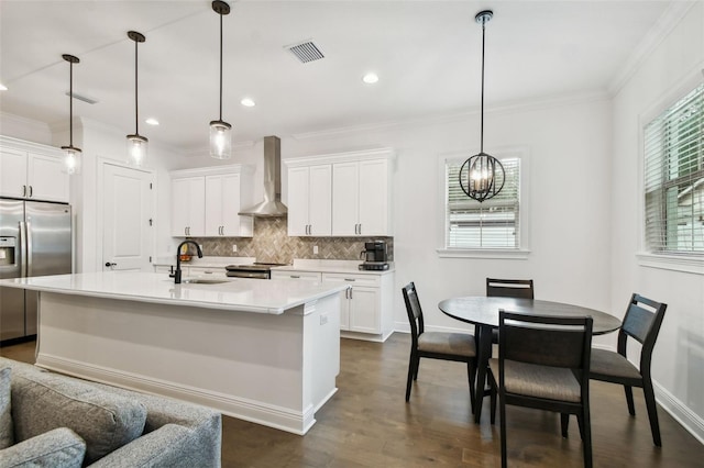 kitchen with an island with sink, white cabinetry, sink, and wall chimney exhaust hood