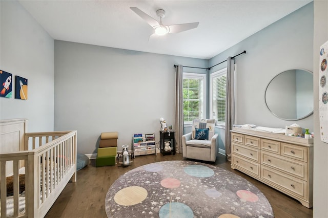 bedroom with a crib, ceiling fan, and dark hardwood / wood-style floors