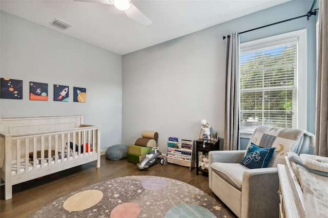 bedroom with dark hardwood / wood-style flooring, ceiling fan, and a nursery area