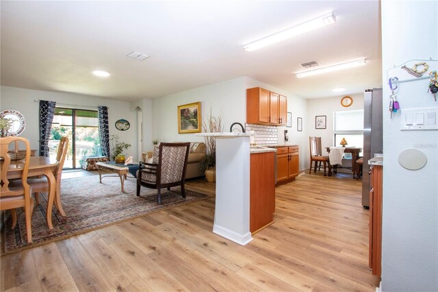 interior space with light hardwood / wood-style flooring, decorative backsplash, stainless steel refrigerator, sink, and kitchen peninsula