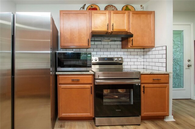 kitchen with stainless steel appliances, light hardwood / wood-style flooring, decorative backsplash, and light stone counters