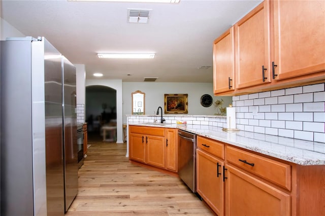 kitchen with sink, appliances with stainless steel finishes, light hardwood / wood-style flooring, light stone counters, and kitchen peninsula