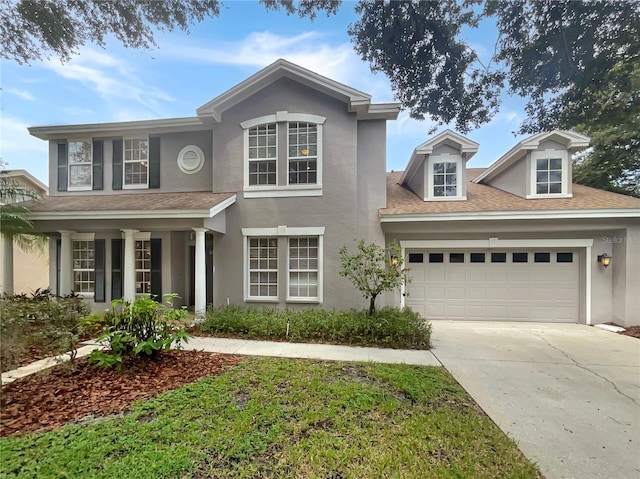 traditional home featuring an attached garage, roof with shingles, concrete driveway, and stucco siding