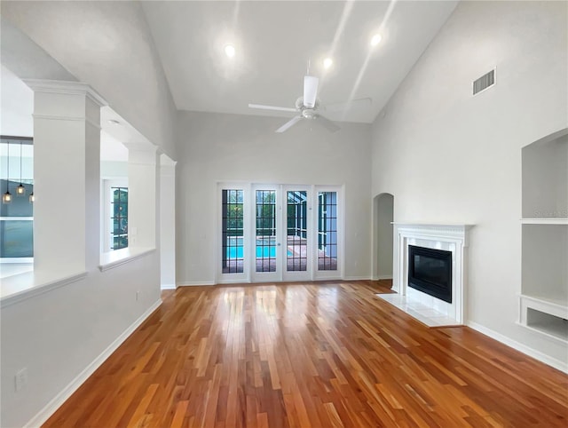 unfurnished living room with visible vents, baseboards, a towering ceiling, light wood-style flooring, and a high end fireplace